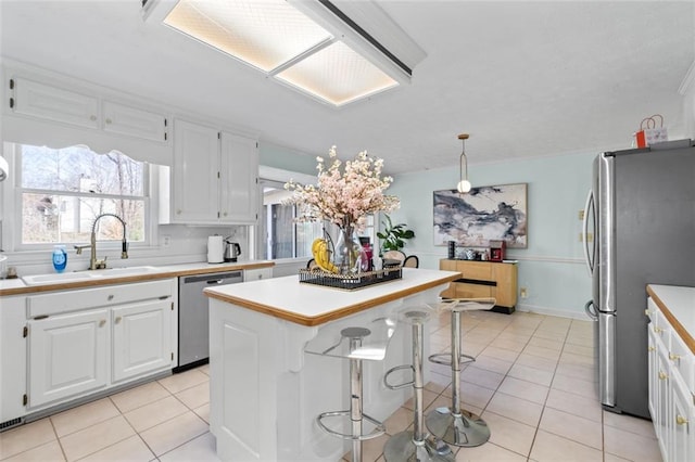 kitchen with light tile patterned floors, appliances with stainless steel finishes, white cabinets, and a sink