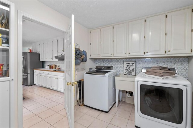 laundry area featuring cabinet space, washing machine and dryer, light tile patterned floors, and a textured ceiling