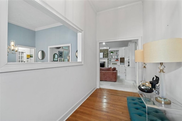 hallway with ornamental molding, an inviting chandelier, wood finished floors, and baseboards