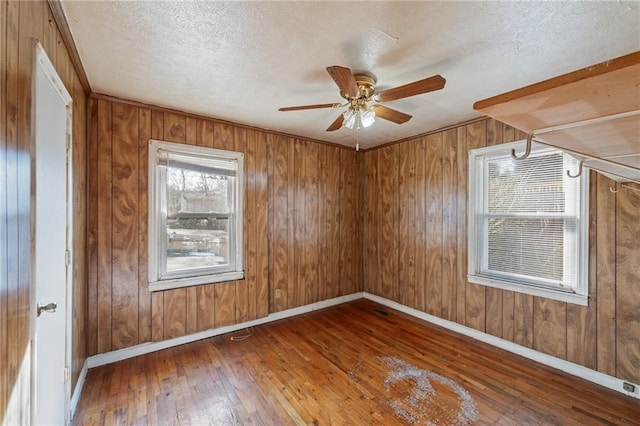 unfurnished room featuring ceiling fan, wood walls, hardwood / wood-style floors, and a healthy amount of sunlight