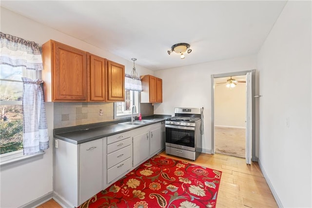 kitchen featuring stainless steel gas range, tasteful backsplash, light wood-type flooring, ceiling fan, and sink