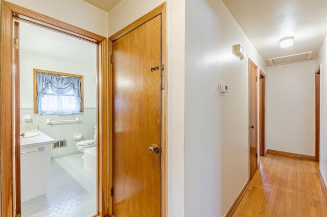 hall with sink, tile walls, and light wood-type flooring