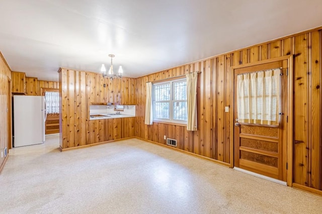 kitchen with pendant lighting, wooden walls, an inviting chandelier, and white refrigerator