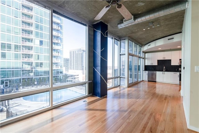 unfurnished living room with a city view, light wood-style flooring, a sink, expansive windows, and ceiling fan