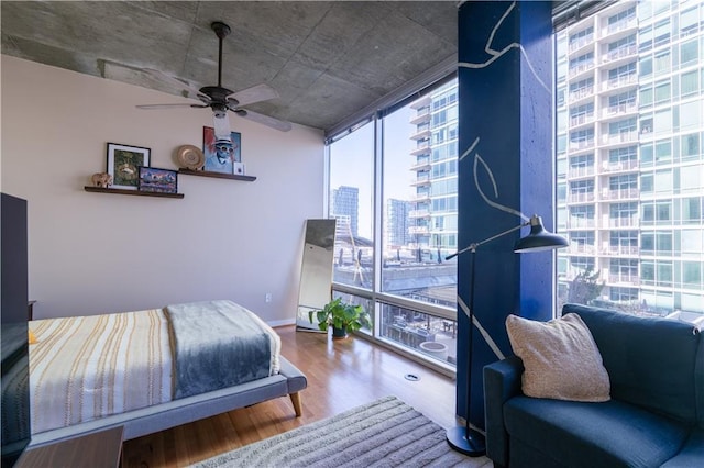 bedroom with baseboards, a city view, floor to ceiling windows, wood finished floors, and a ceiling fan