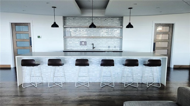 bar with hanging light fixtures, dark wood-style floors, and a sink