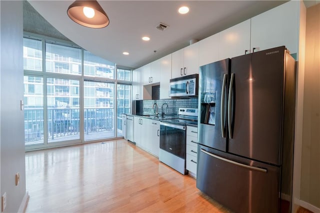 kitchen featuring visible vents, light wood-style flooring, decorative backsplash, appliances with stainless steel finishes, and expansive windows