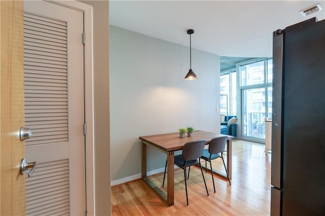 dining room with light wood finished floors, visible vents, a wall of windows, and baseboards