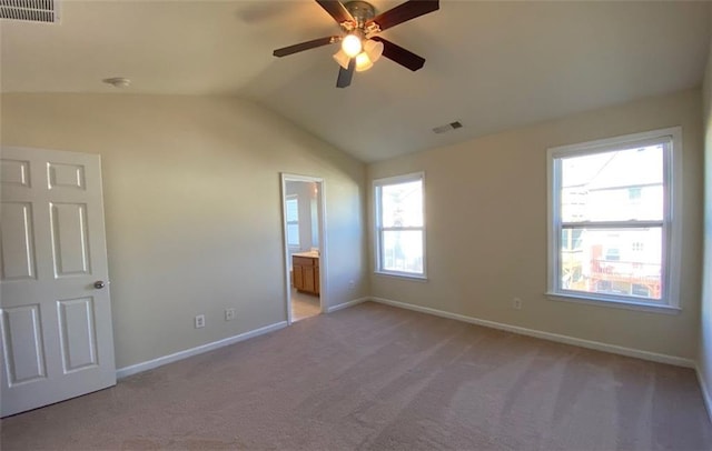 unfurnished bedroom with ensuite bath, multiple windows, lofted ceiling, and light colored carpet