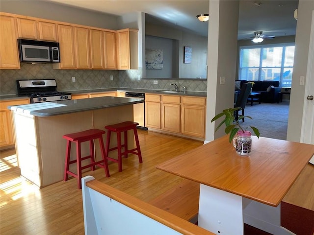 kitchen with ceiling fan, light hardwood / wood-style floors, a kitchen bar, a kitchen island, and appliances with stainless steel finishes