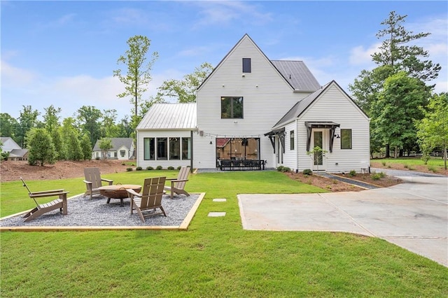 back of property with a lawn, an outdoor fire pit, metal roof, and a patio area