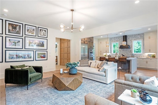 living room featuring an inviting chandelier, baseboards, light wood-style floors, and recessed lighting