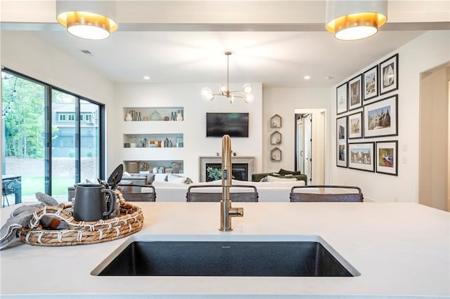 kitchen with visible vents, light countertops, a sink, a glass covered fireplace, and an inviting chandelier