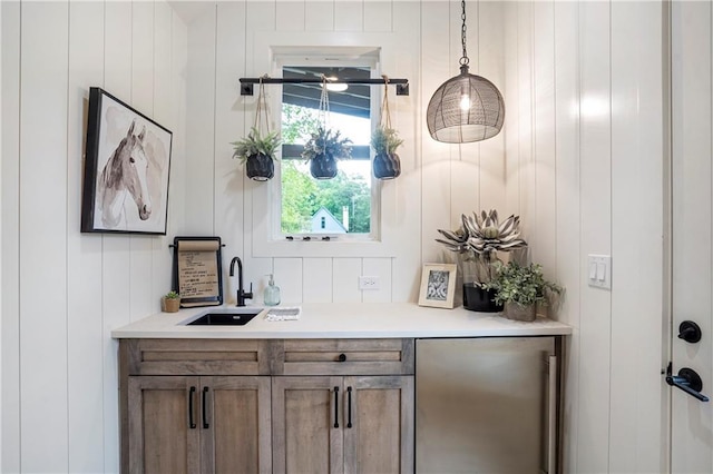 bar with a sink, hanging light fixtures, and freestanding refrigerator
