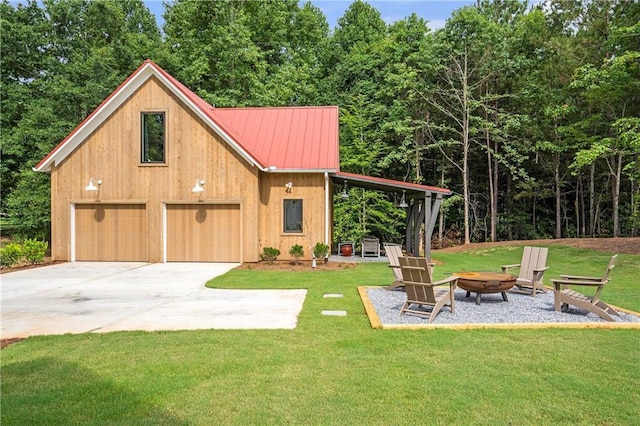 view of front of home with metal roof, concrete driveway, a fire pit, and a front lawn