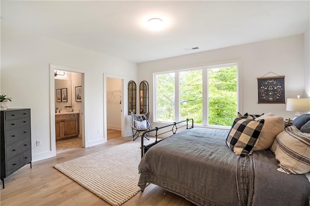 bedroom featuring ensuite bath, baseboards, visible vents, and light wood-style floors