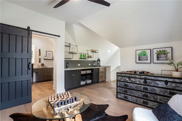 living room featuring lofted ceiling, indoor wet bar, a barn door, a ceiling fan, and light wood finished floors
