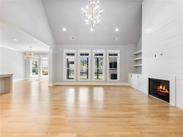 unfurnished living room with a high ceiling, built in shelves, an inviting chandelier, and light hardwood / wood-style floors