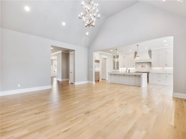 unfurnished living room featuring high vaulted ceiling, a chandelier, and light wood-type flooring