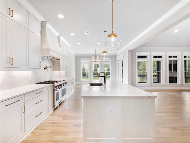 kitchen with sink, custom range hood, white cabinetry, and range with two ovens