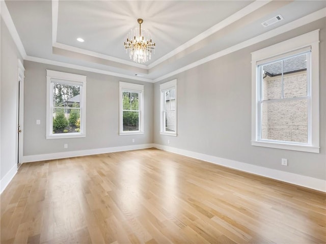 spare room featuring a raised ceiling, a chandelier, ornamental molding, and light hardwood / wood-style flooring