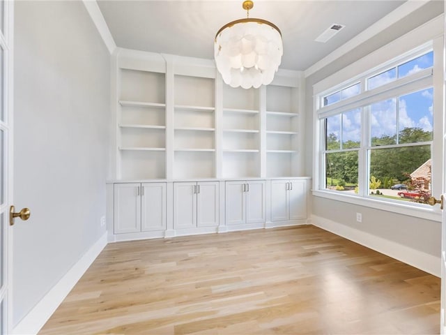 empty room with light wood-type flooring, built in features, and a notable chandelier