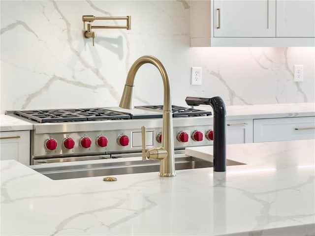 room details featuring white cabinets, stainless steel range, light stone counters, and decorative backsplash