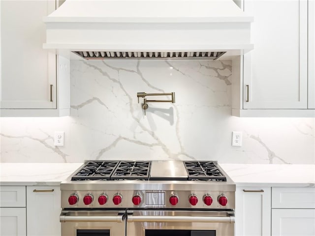 kitchen featuring custom exhaust hood, tasteful backsplash, range with two ovens, and light stone counters