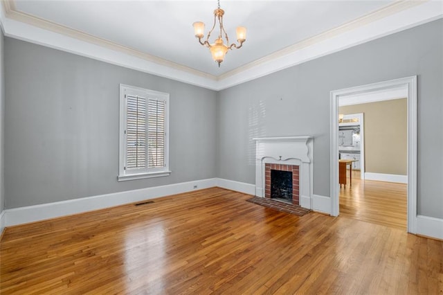 unfurnished living room featuring light wood-type flooring, crown molding, a notable chandelier, and a brick fireplace