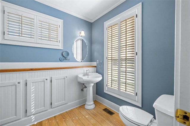 bathroom with wood-type flooring, crown molding, toilet, and a wealth of natural light