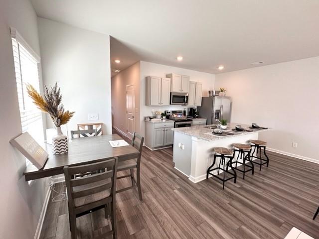 kitchen with dark wood-style flooring, a center island with sink, recessed lighting, appliances with stainless steel finishes, and a kitchen breakfast bar