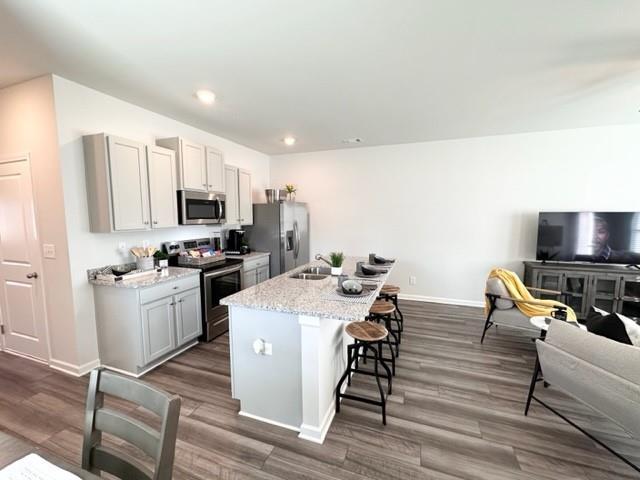 kitchen featuring a breakfast bar area, baseboards, open floor plan, appliances with stainless steel finishes, and an island with sink