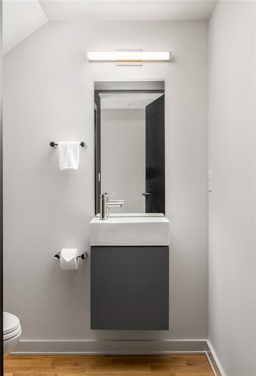 bathroom featuring vanity, lofted ceiling, wood-type flooring, and toilet