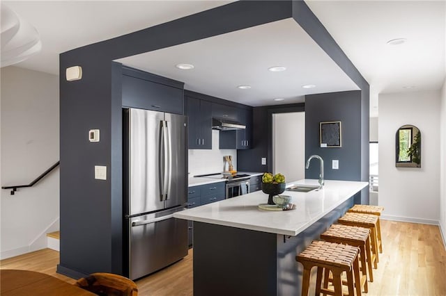 kitchen with stainless steel appliances, a kitchen island with sink, a breakfast bar area, and light hardwood / wood-style flooring