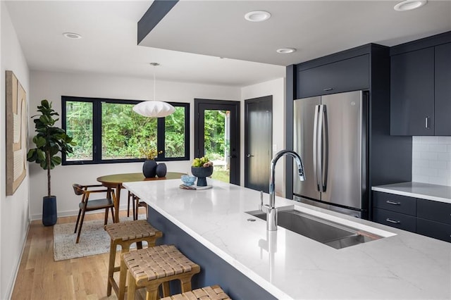 kitchen with decorative light fixtures, sink, stainless steel fridge, a kitchen bar, and light stone counters