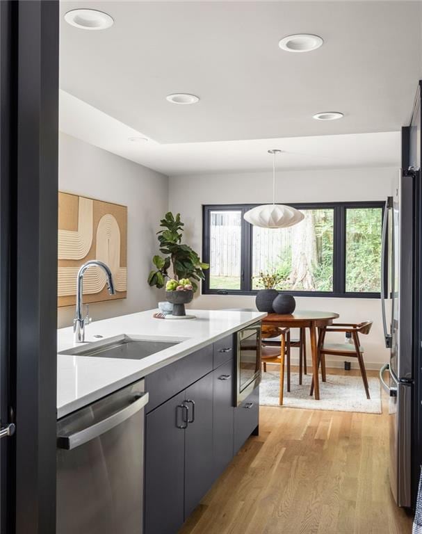 kitchen featuring sink, hanging light fixtures, light wood-type flooring, plenty of natural light, and appliances with stainless steel finishes