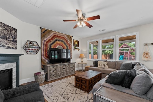 living area featuring a ceiling fan, baseboards, light wood finished floors, and a fireplace