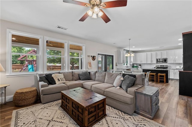 living area featuring light wood-style floors, a ceiling fan, recessed lighting, and a chandelier