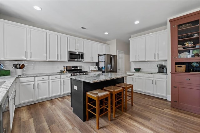 kitchen with stainless steel appliances, wood finished floors, white cabinets, and recessed lighting