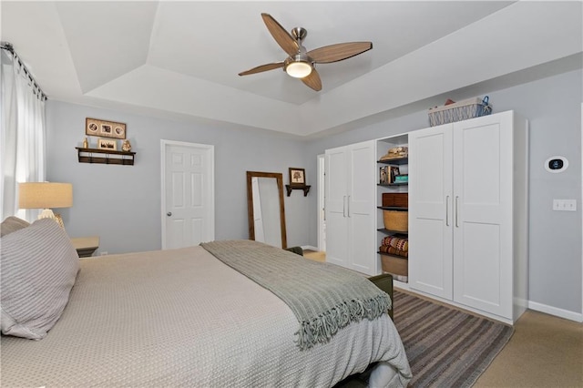 bedroom featuring a tray ceiling, baseboards, carpet flooring, and a ceiling fan
