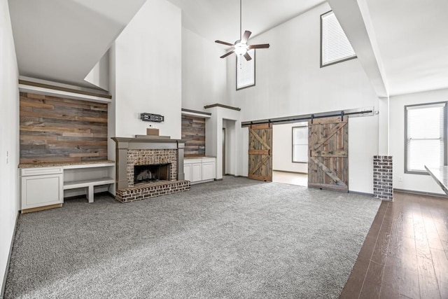 unfurnished living room featuring wooden walls, ceiling fan, a fireplace, a barn door, and dark hardwood / wood-style flooring