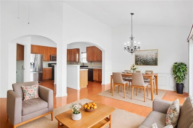 living area featuring arched walkways, light wood-style flooring, a high ceiling, and a chandelier