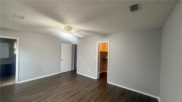 unfurnished bedroom with dark wood-type flooring, ensuite bathroom, a walk in closet, ceiling fan, and a closet