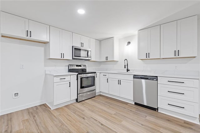 6142 Hutchins Dr, Buford, GA 30518 - kitchen with stainless steel appliances, a sink, light wood-style floors, white cabinetry, and baseboards