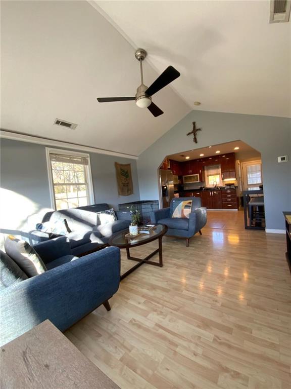 living room featuring light wood-type flooring, high vaulted ceiling, visible vents, and arched walkways