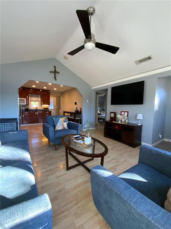 living area featuring vaulted ceiling, arched walkways, and light wood-style flooring