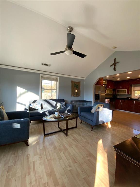 living area with vaulted ceiling, light wood finished floors, visible vents, and a ceiling fan