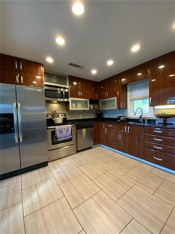 kitchen with appliances with stainless steel finishes, dark countertops, a sink, and visible vents