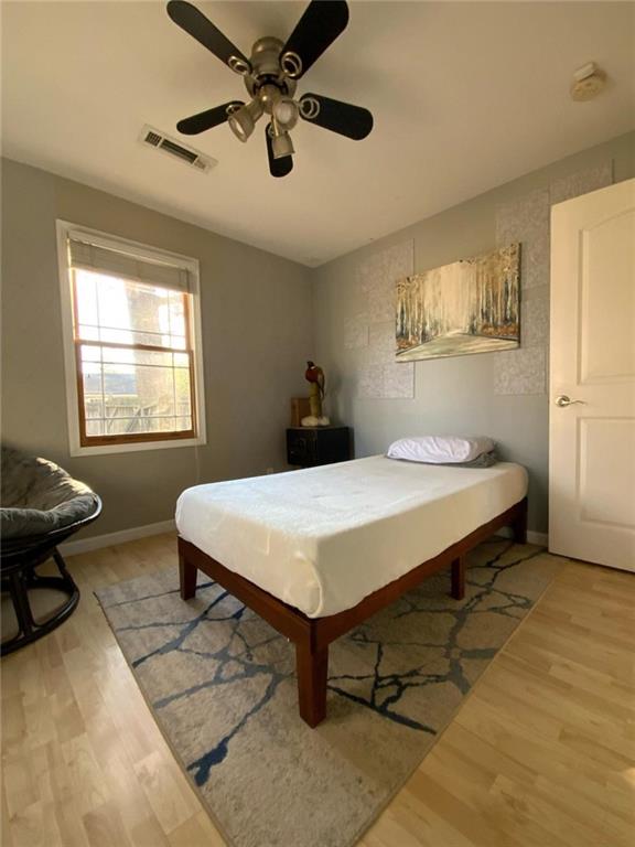 bedroom with a ceiling fan, light wood-type flooring, visible vents, and baseboards