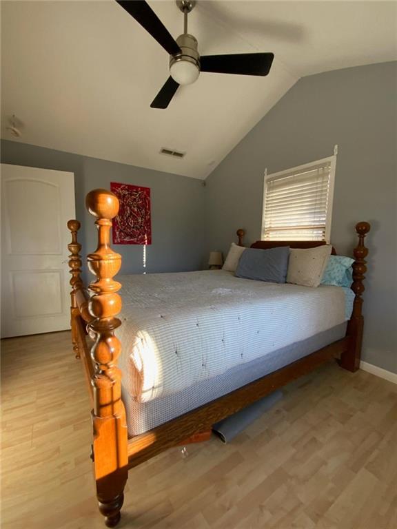 bedroom with ceiling fan, visible vents, vaulted ceiling, and wood finished floors